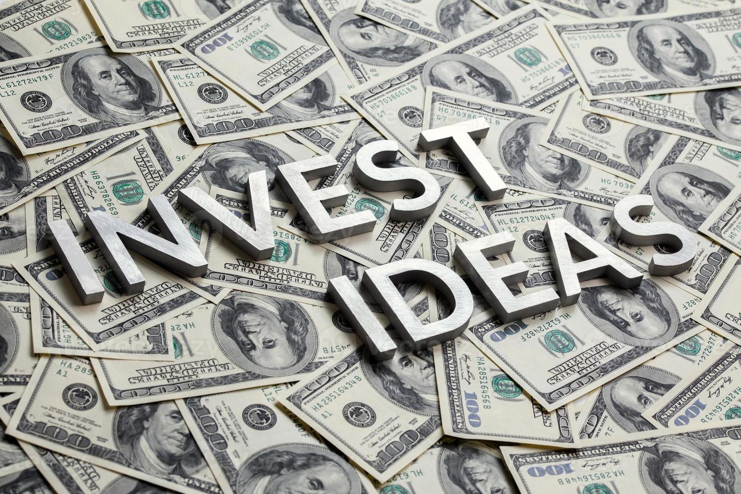The words INVEST IDEAS with thick metal letters on the US dollar bills background - with selective focus photo