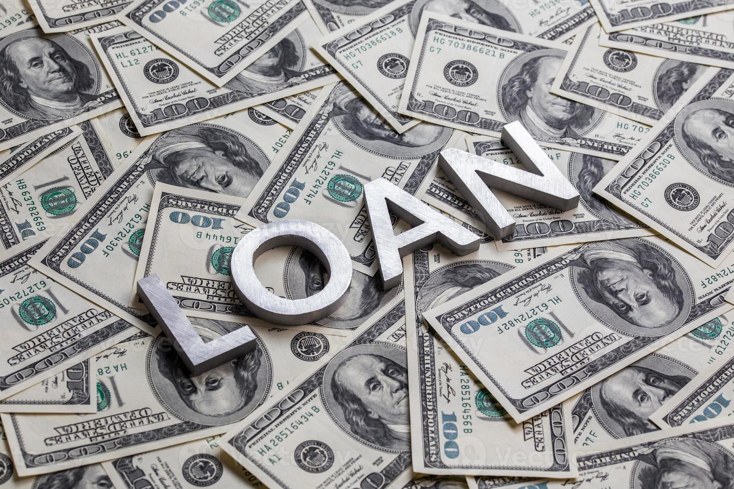 The word LOAN laid with aluminium letters on the US dollar banknotes background - with selective focus photo