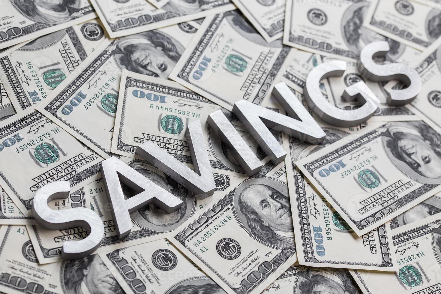 The word SAVINGS laid with white metal letters on the americal dollar banknotes background with selective focus photo