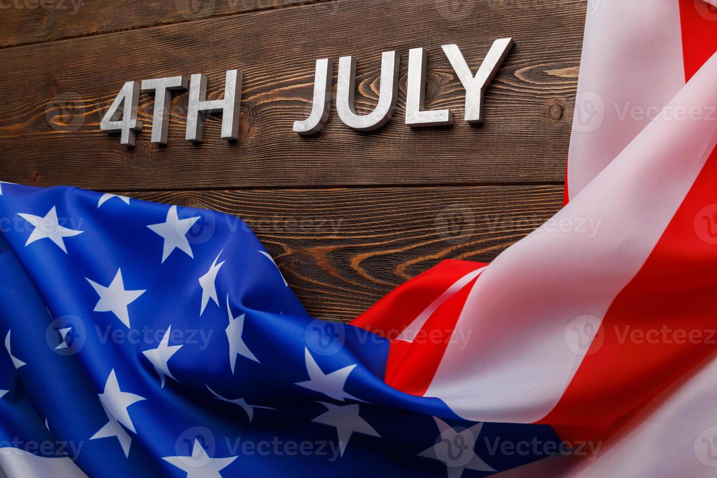 the words 4th july and crumpled usa flag on flat textured wooden surface background photo