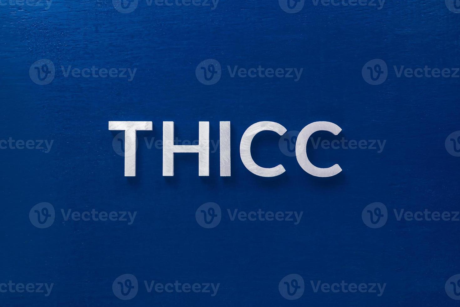 the word thicc laid with silver metal letters on classic blue board in flat lay with central composition photo