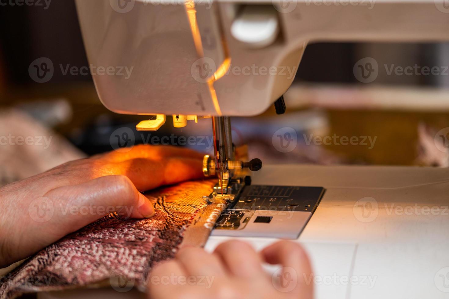 a close-up view of sewing process, hand of old woman using sewing machine, selective focus technique photo