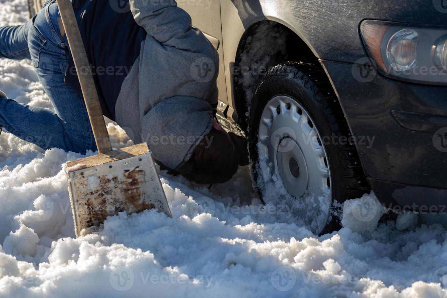 man working at car stuck in snow on knee with shovel at daylight offroad photo