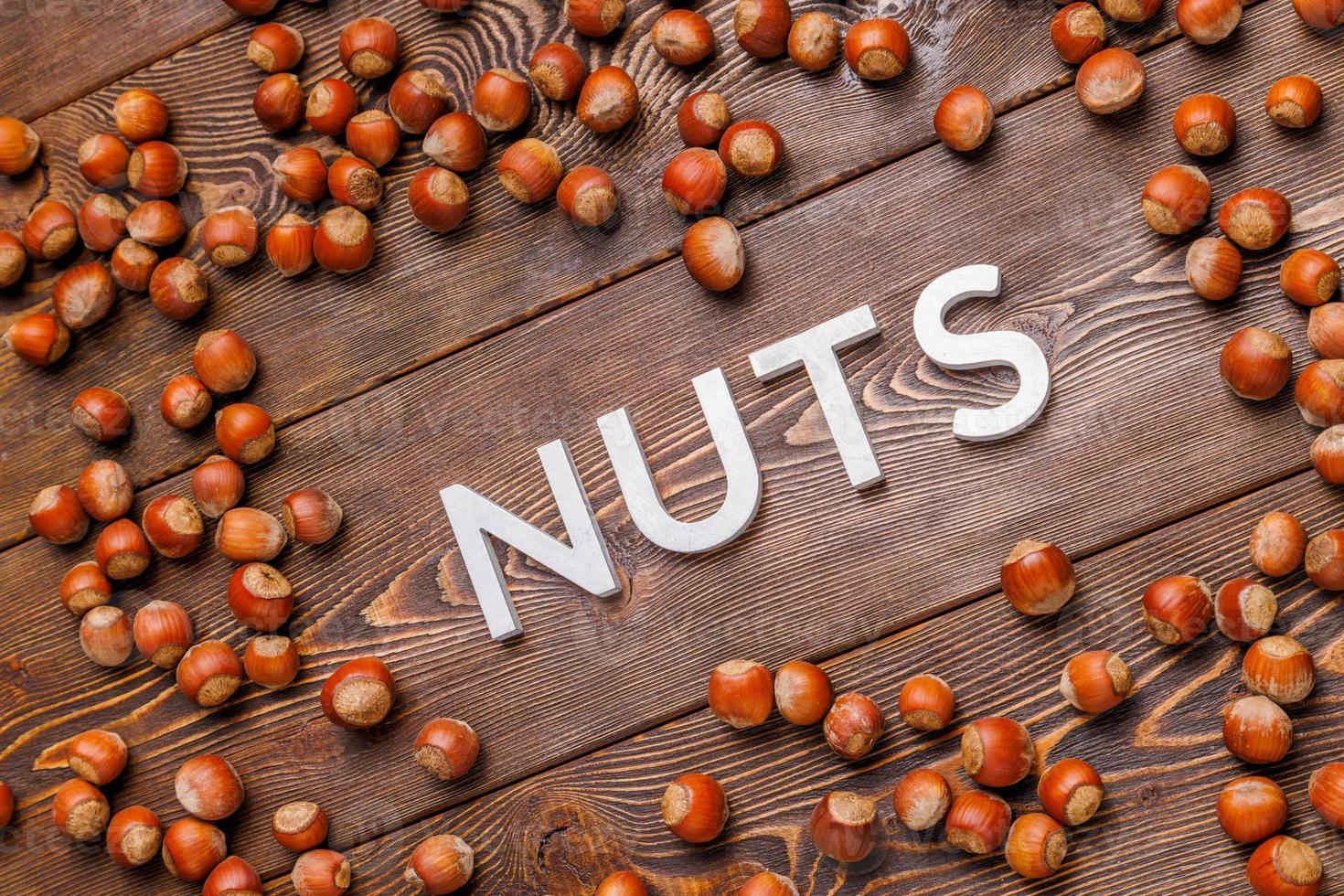 la palabra nueces colocada con letras plateadas sobre fondo de tablero de madera rodeada de avellanas dispersas foto