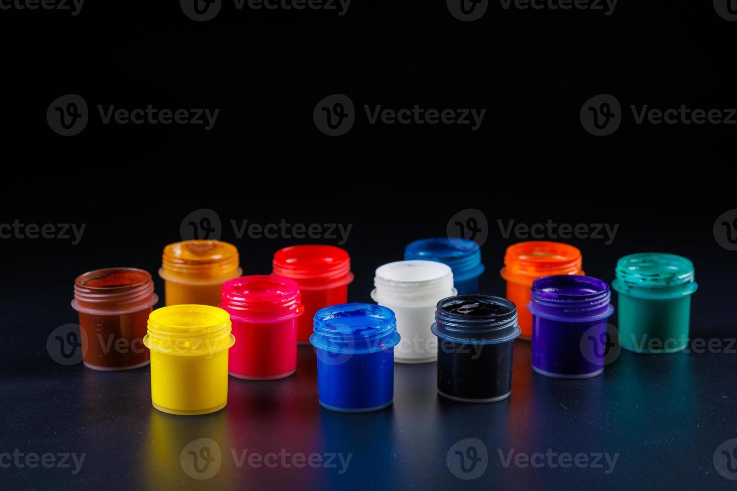 close-up background of opened small gouache paint jars on black surface photo