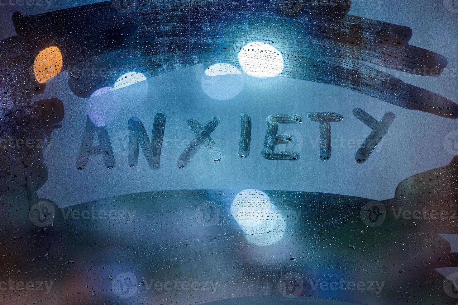 the word anxiety handwritten on night wet glass with classic blue lights in background photo