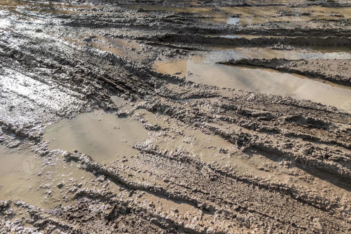 dirty clay mud road with tire tracks at day time - full frame background with hard sun light photo