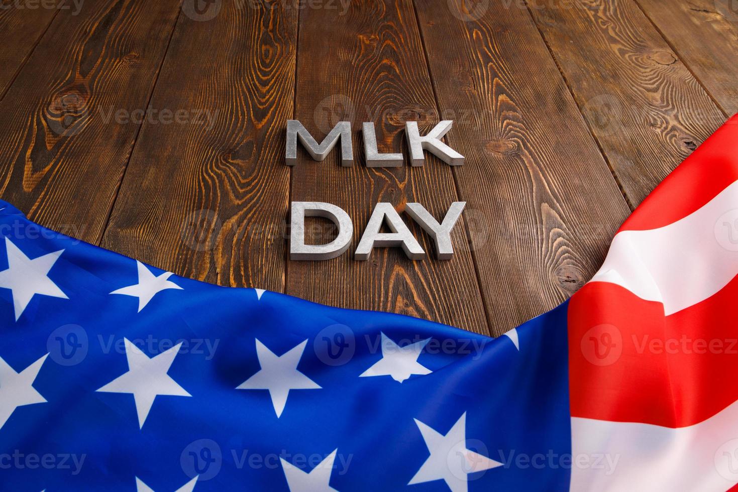 la palabra mlk day colocada con letras de metal plateado sobre una superficie de madera con una bandera de estados unidos arrugada debajo foto