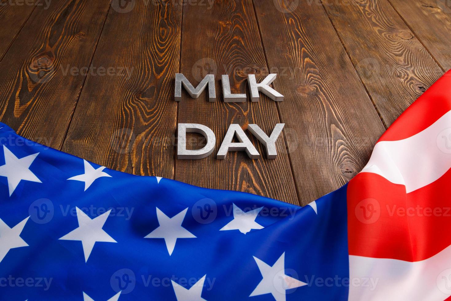 the word MLK day laid with silver metal letters on wooden surface with crumpled USA flag underneath photo