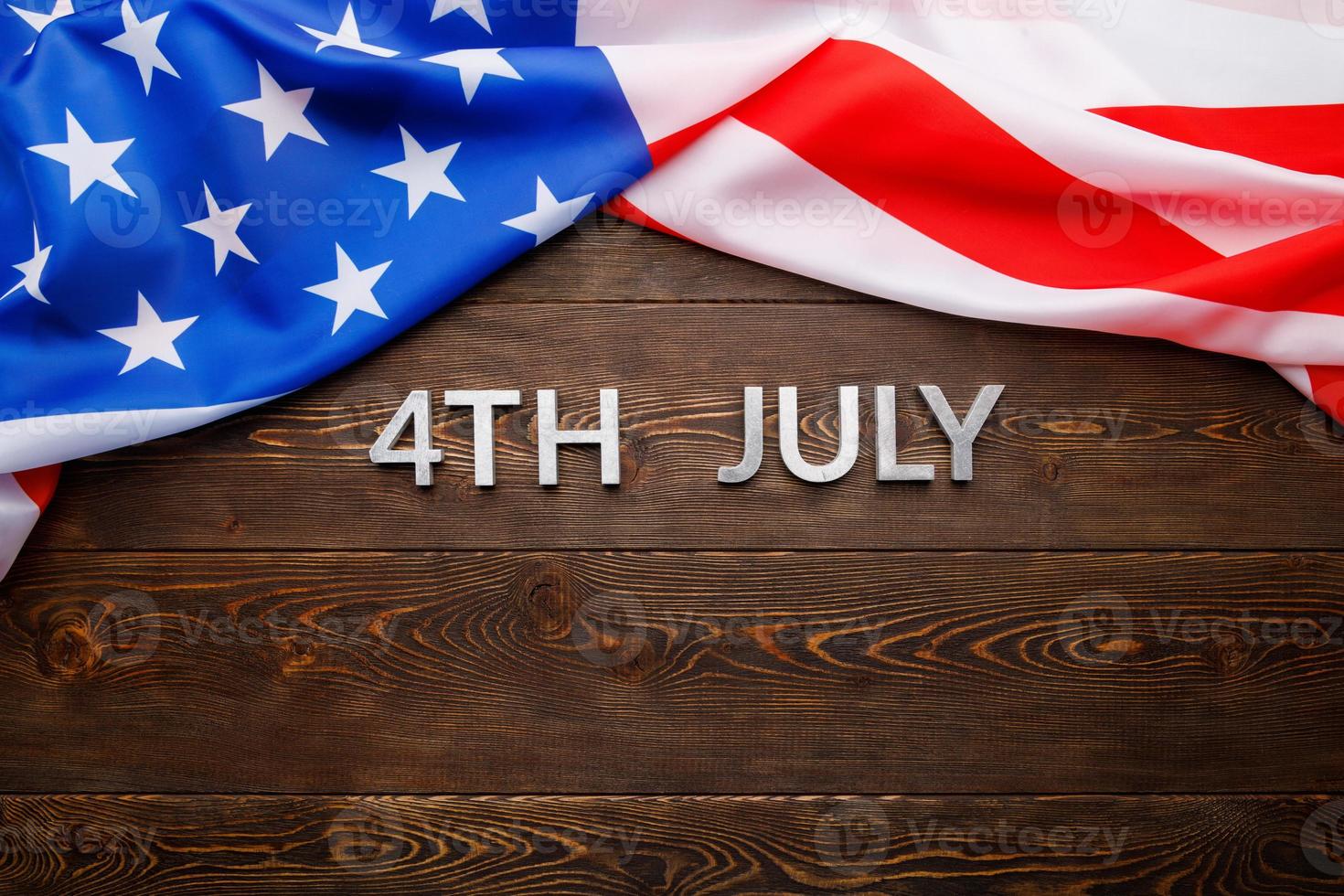 the words 4th july and crumpled usa flag on flat textured wooden surface background photo