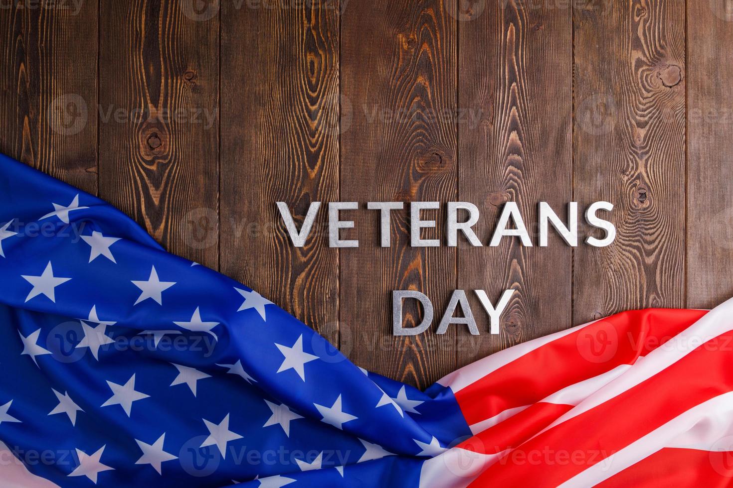 the words veterans day laid with silver metal letters on wooden board surface with crumpled usa flag photo