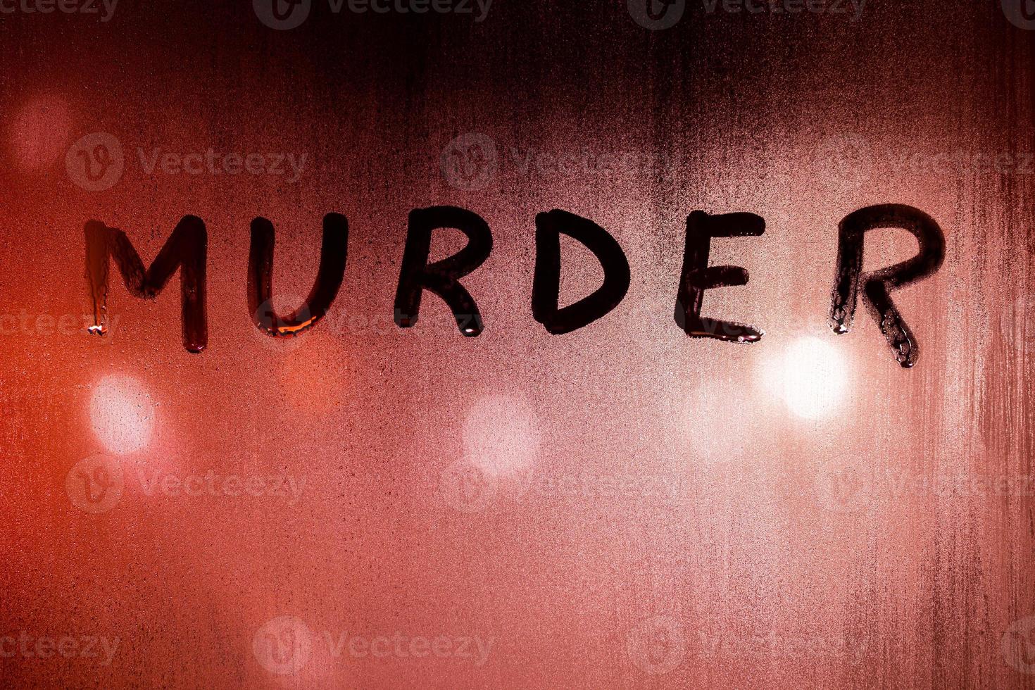 the word murder handwritten on wet glass of night window with bloody red back light of street lights photo