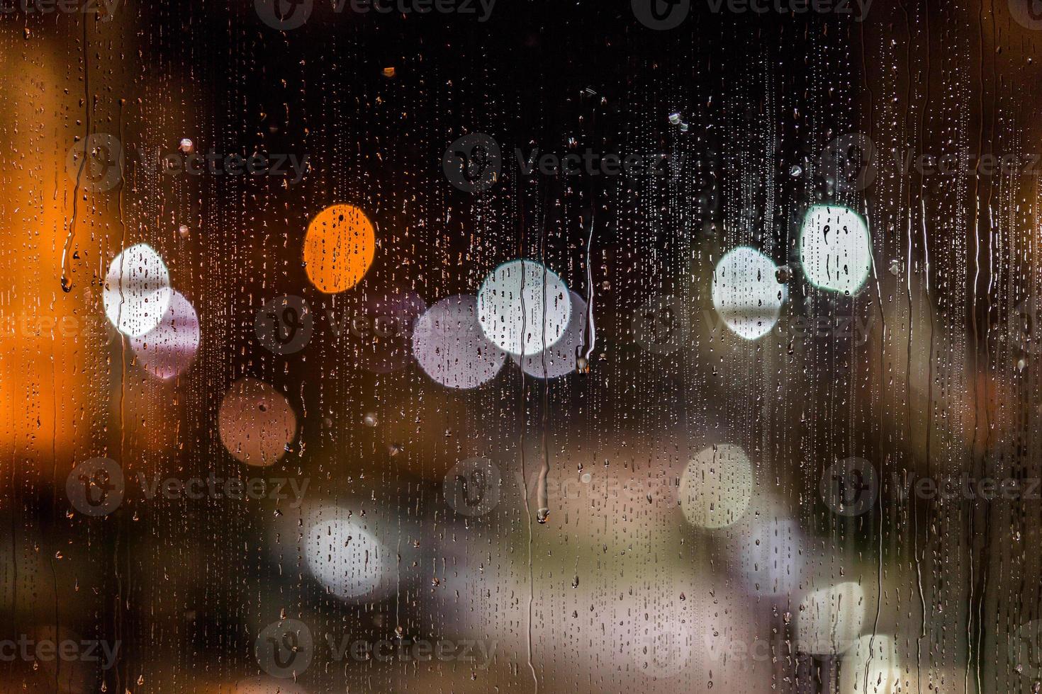 an abstract background night street lights bokeh through wet glass with water smudges, close-up with selective focus photo