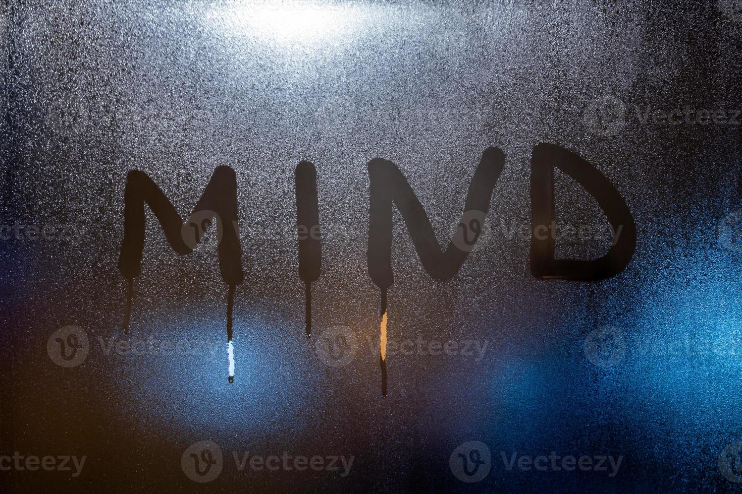 the word mind written on night wet window glass close-up with blurred background photo