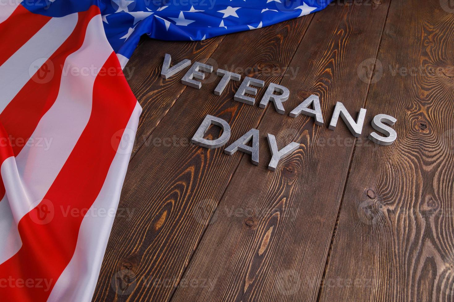 the words veterans day laid with silver metal letters on wooden board surface with crumpled usa flag photo