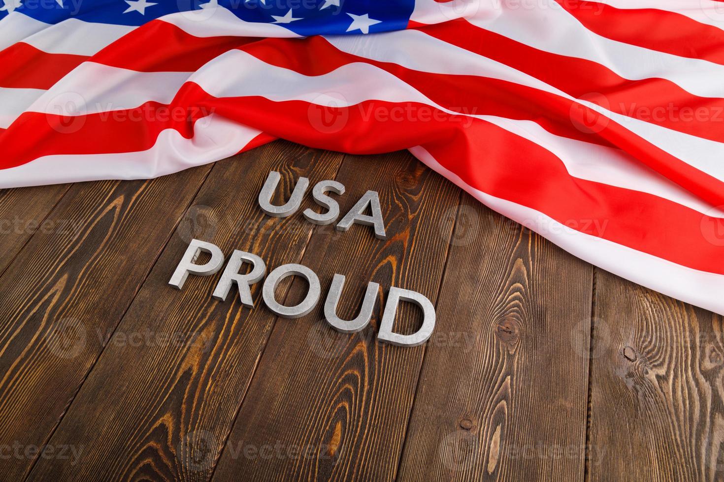 words USA proud laid with silver metal letters on brown wooden surface with flag of United States of America photo