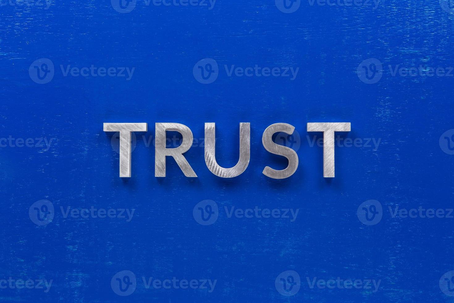 the word trust laid with silver metal characters on blue painted wooden board in central flat lay composition photo