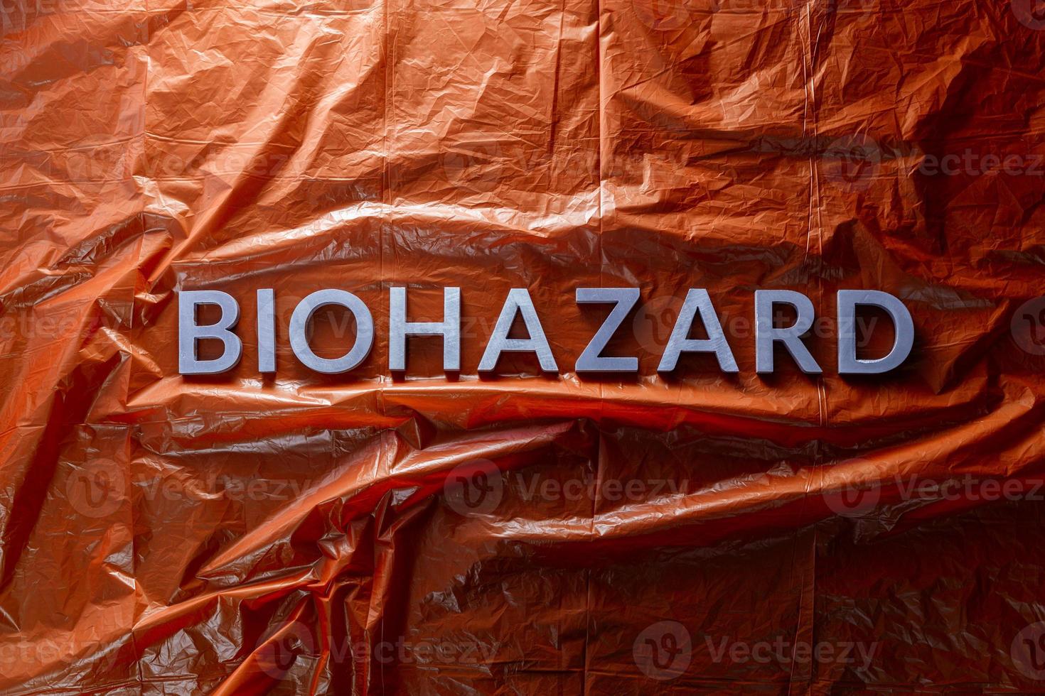 the word biohazard laid with silver letters on red crumpled plastic film background in flat lay composition at center photo