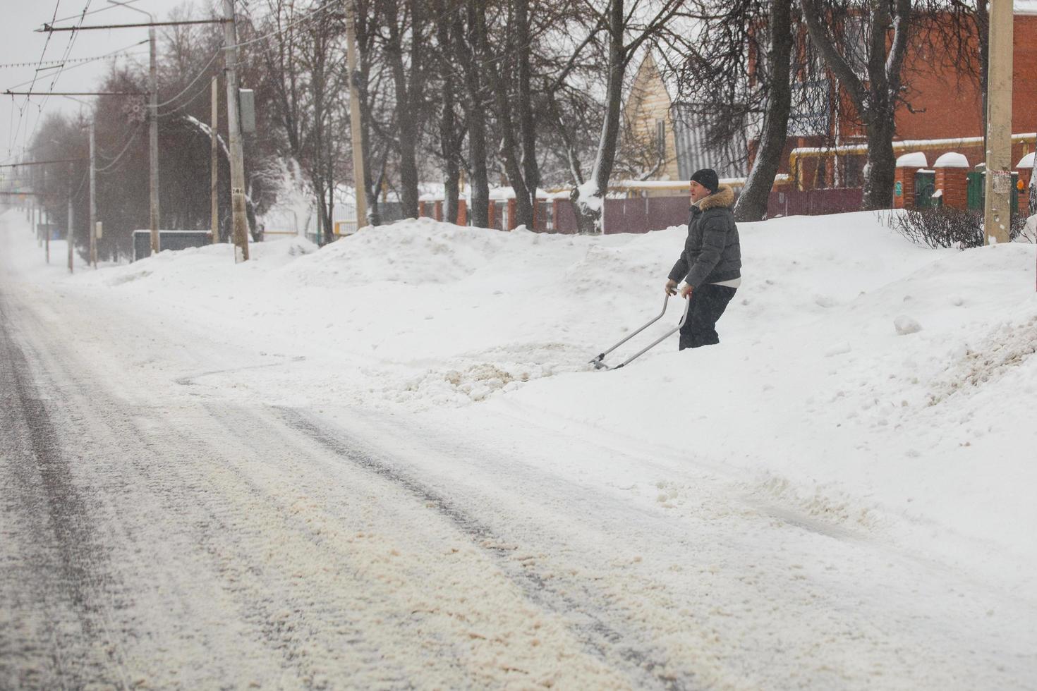 tula, rusia 13 de febrero de 2020 hombre limpiando la calzada con raspador de nieve en la mañana de invierno después de la tormenta de nieve. foto