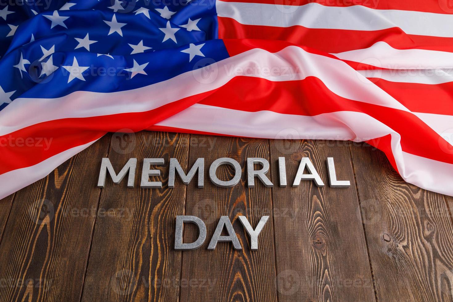 the words memorial day laid with silver metal letters on wooden board surface with crumpled usa flag above photo