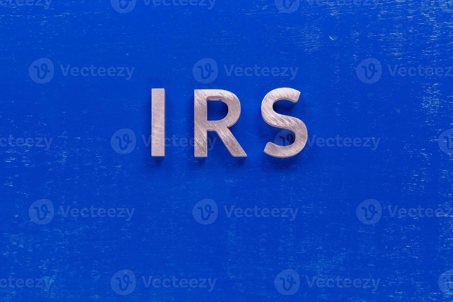 the word irs layed on blue painted board with thick silver metal aphabet characters photo