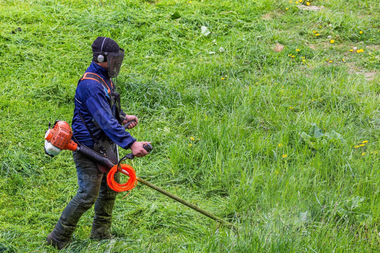 lawnmower man with string trimmer and face mask trimmong grass - close-up photo