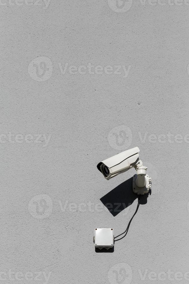 small white surveillance camera on flat gray matte plaster wall photo