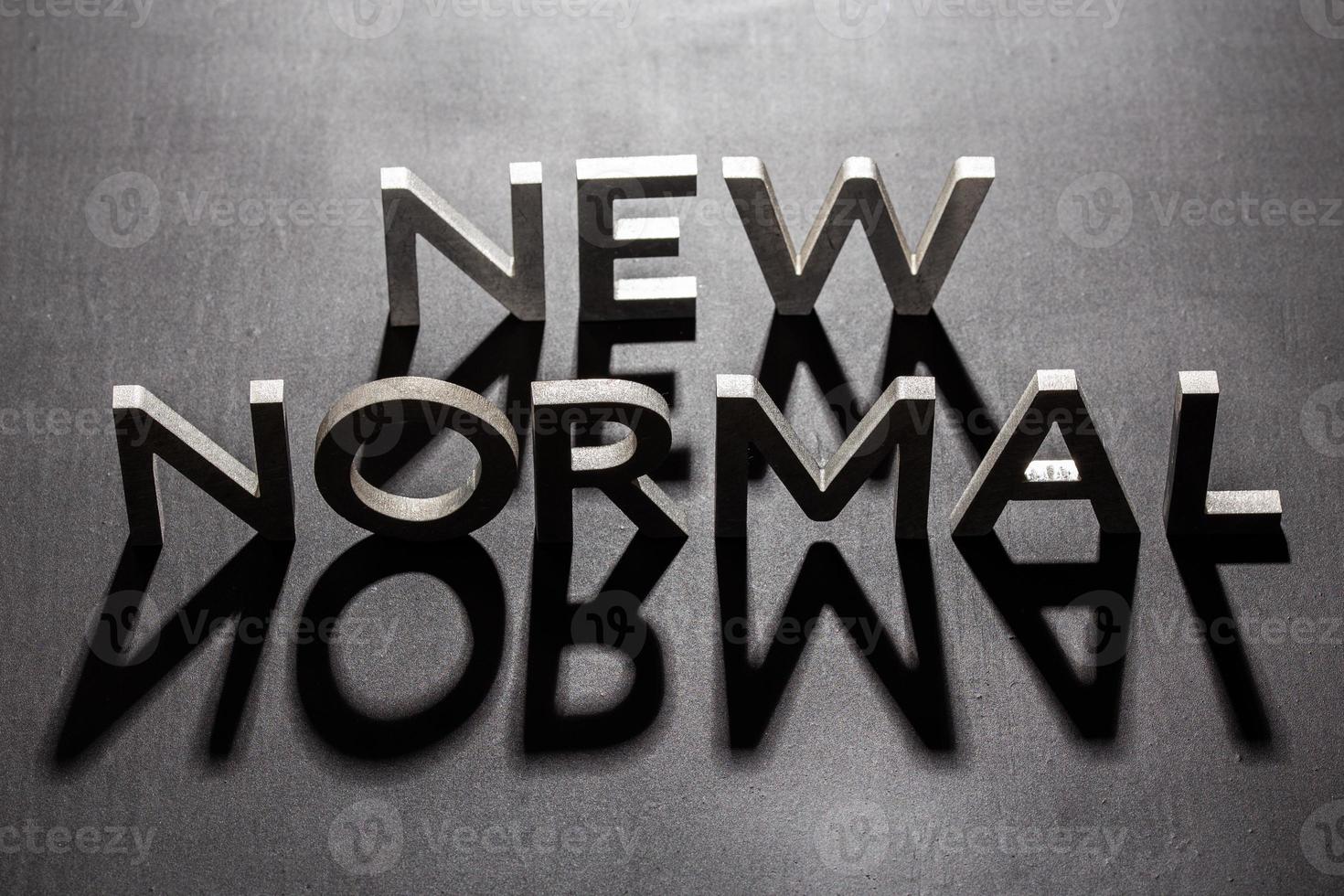 new normal word composed of silver metal letters on a flat matt black surface with shadows backlit photo
