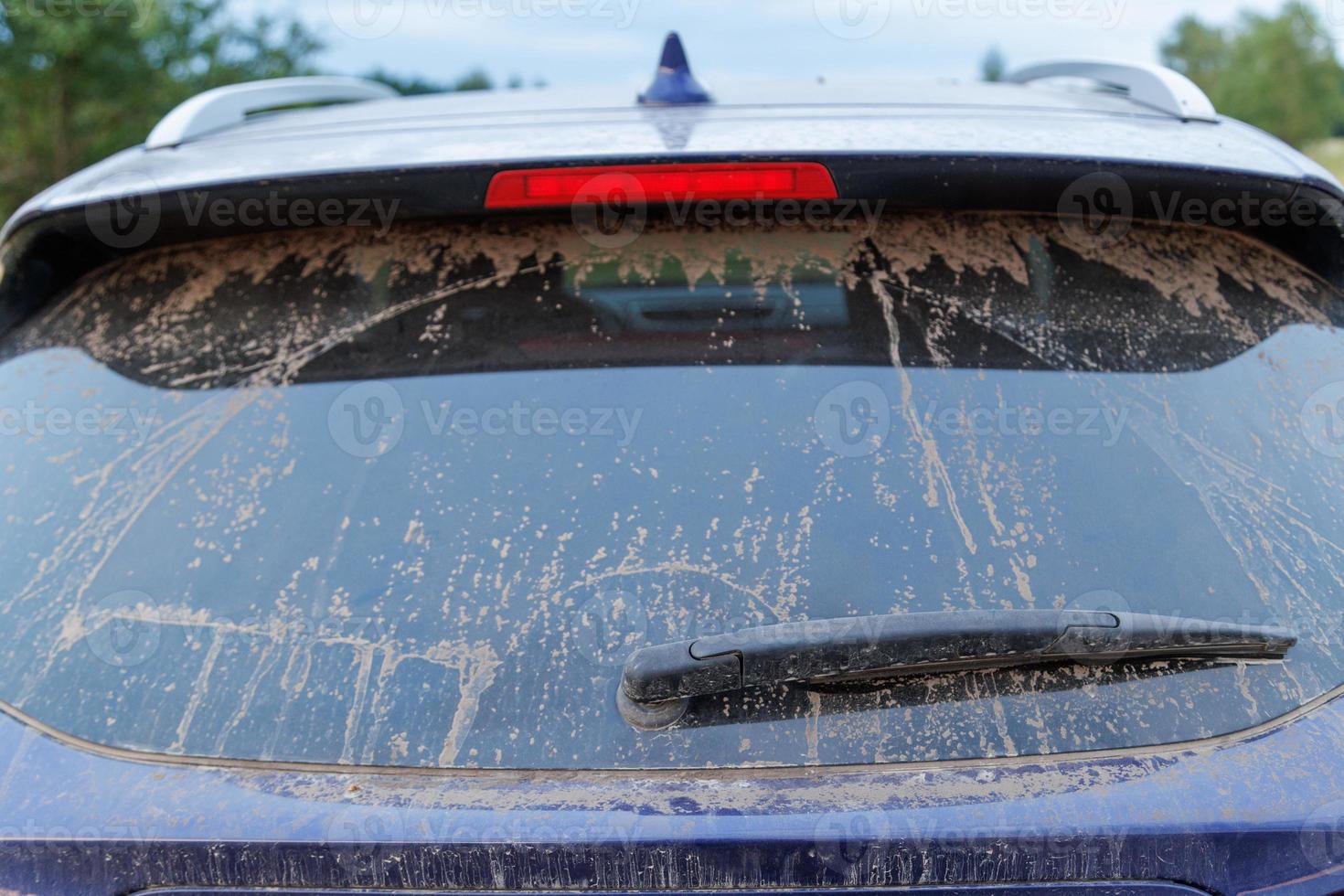 Dirty car glass with wiper and third brake light, rear window covered with a layer of dust. photo