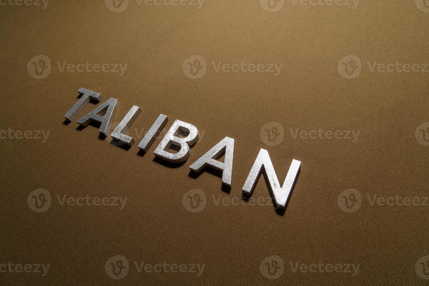 the word taliban laid with silver metal letters on rough tan khaki canvas fabric photo