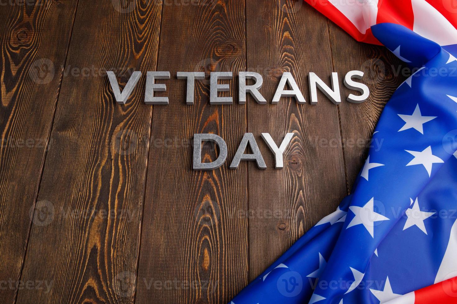 the words veterans day laid with silver metal letters on wooden board surface with crumpled usa flag photo