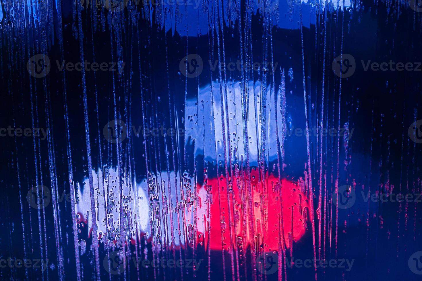 an abstract background of red and blue police lights bokeh trough wet glass at night close-up with selective focus photo