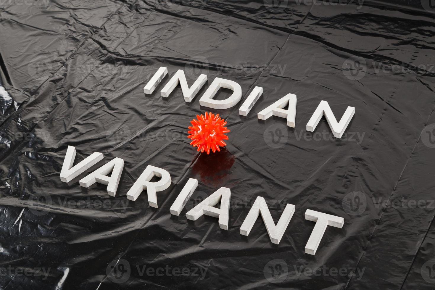 words indian variant laid with silver metal letters on crumpled black plastic bag background with small virus model photo