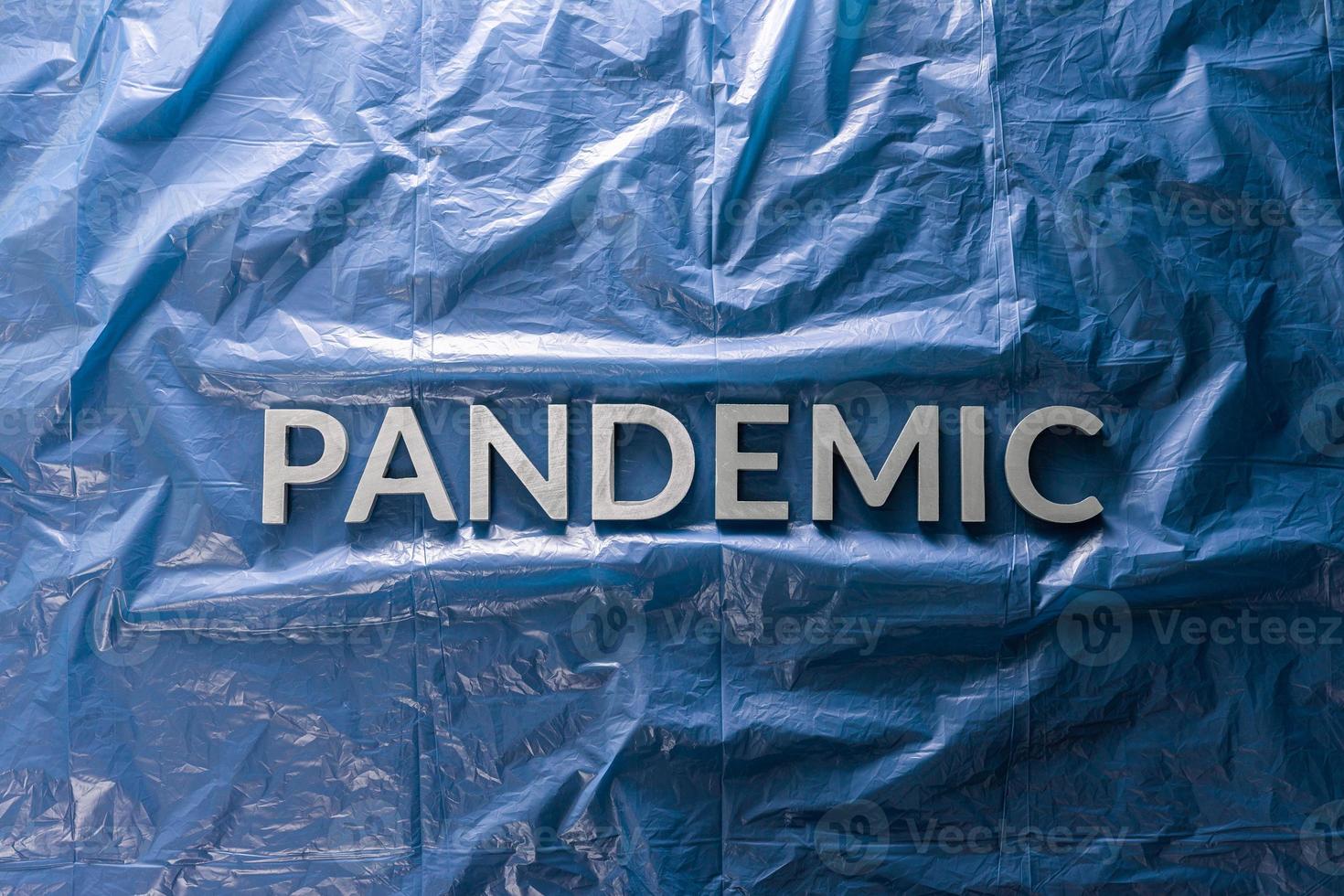 the word pandemic laid with silver letters on crumpled blue plastic film background in flat lay composition at center photo