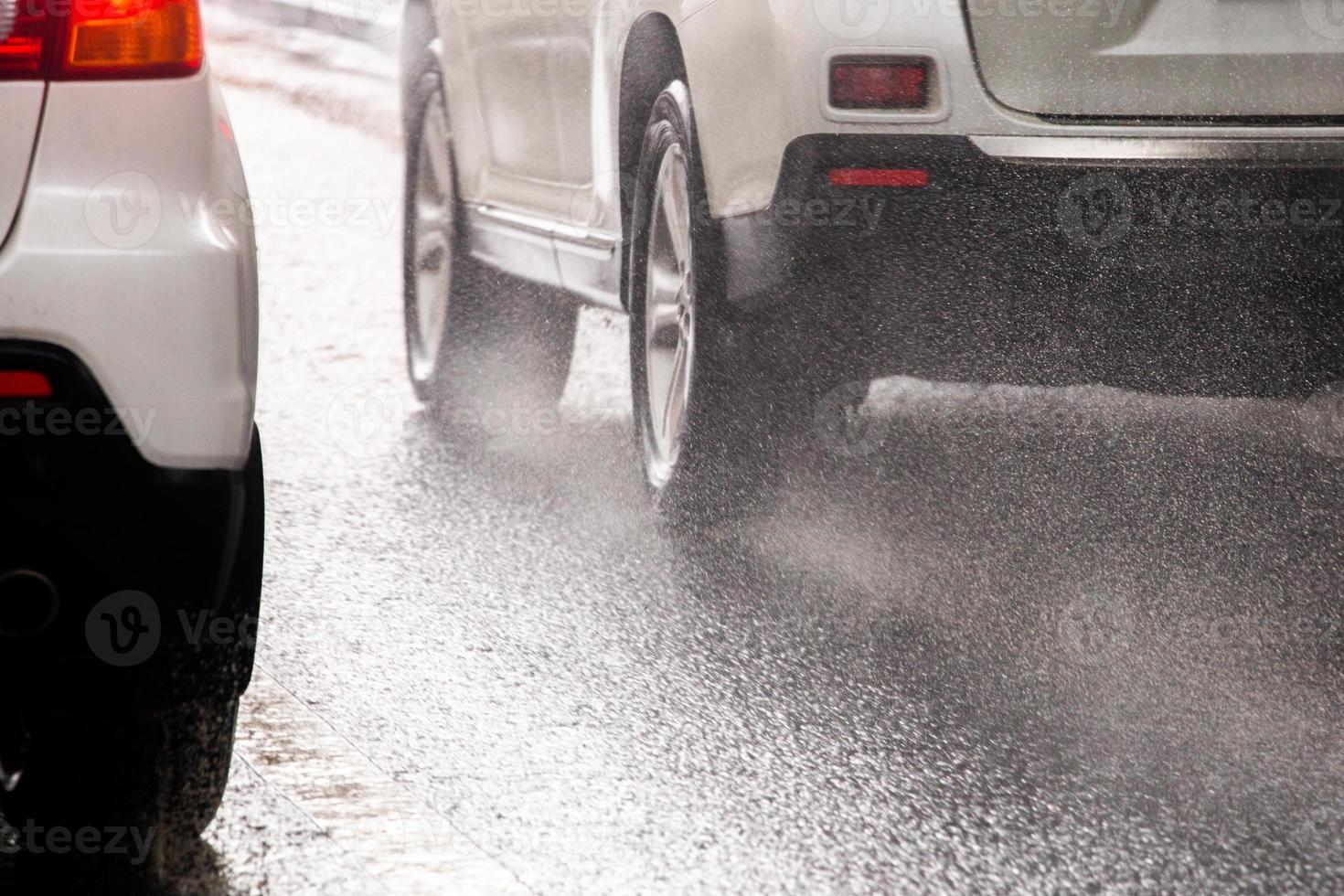 el agua de lluvia salpica el flujo de las ruedas de los autos blancos que se mueven rápido en la ciudad a la luz del día con enfoque selectivo foto