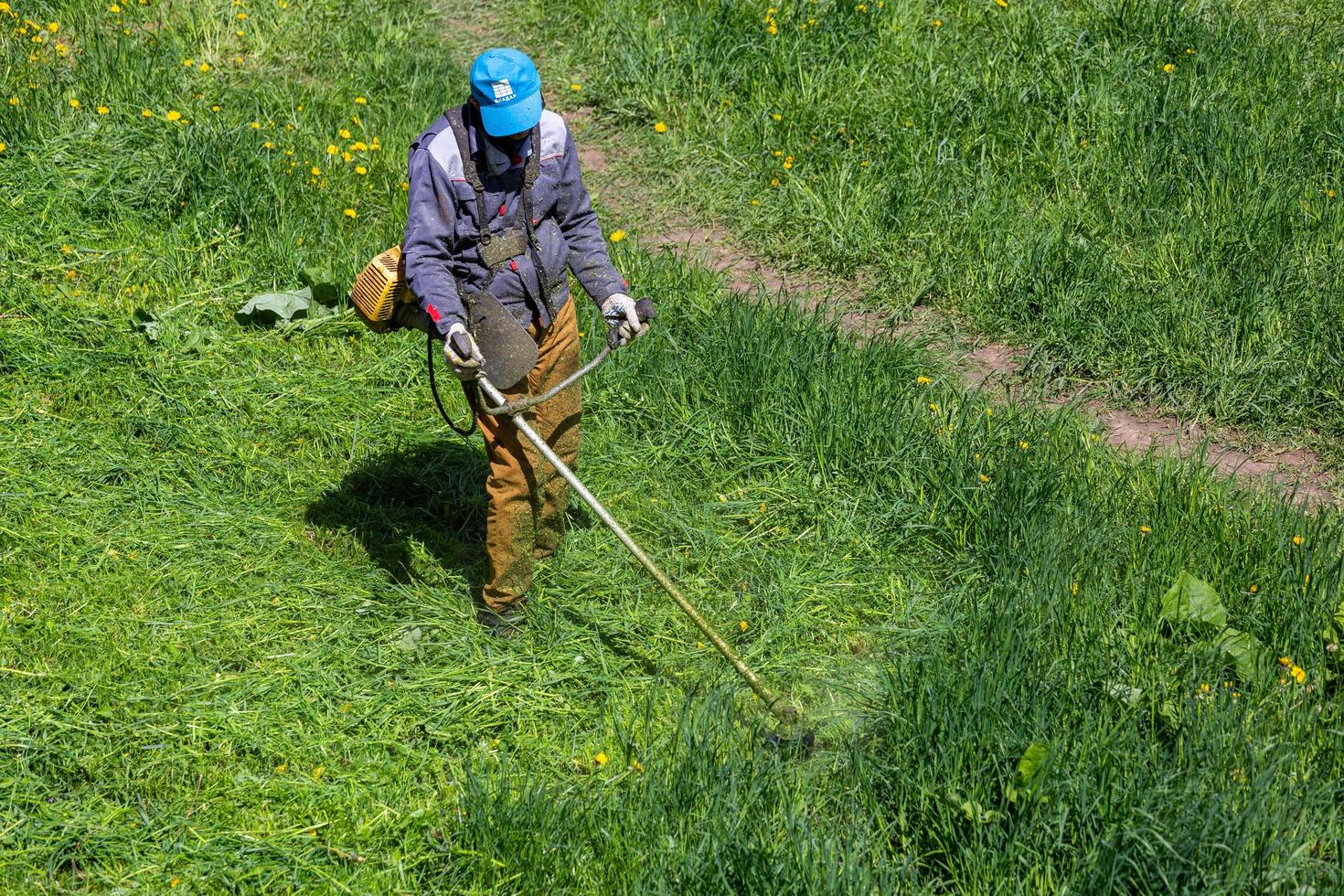 TULA, RUSSIA MAY 19, 2020 Russian official lawnmower worker man cutting green grass with two-cycle engine string trimmer. Top to down view. photo