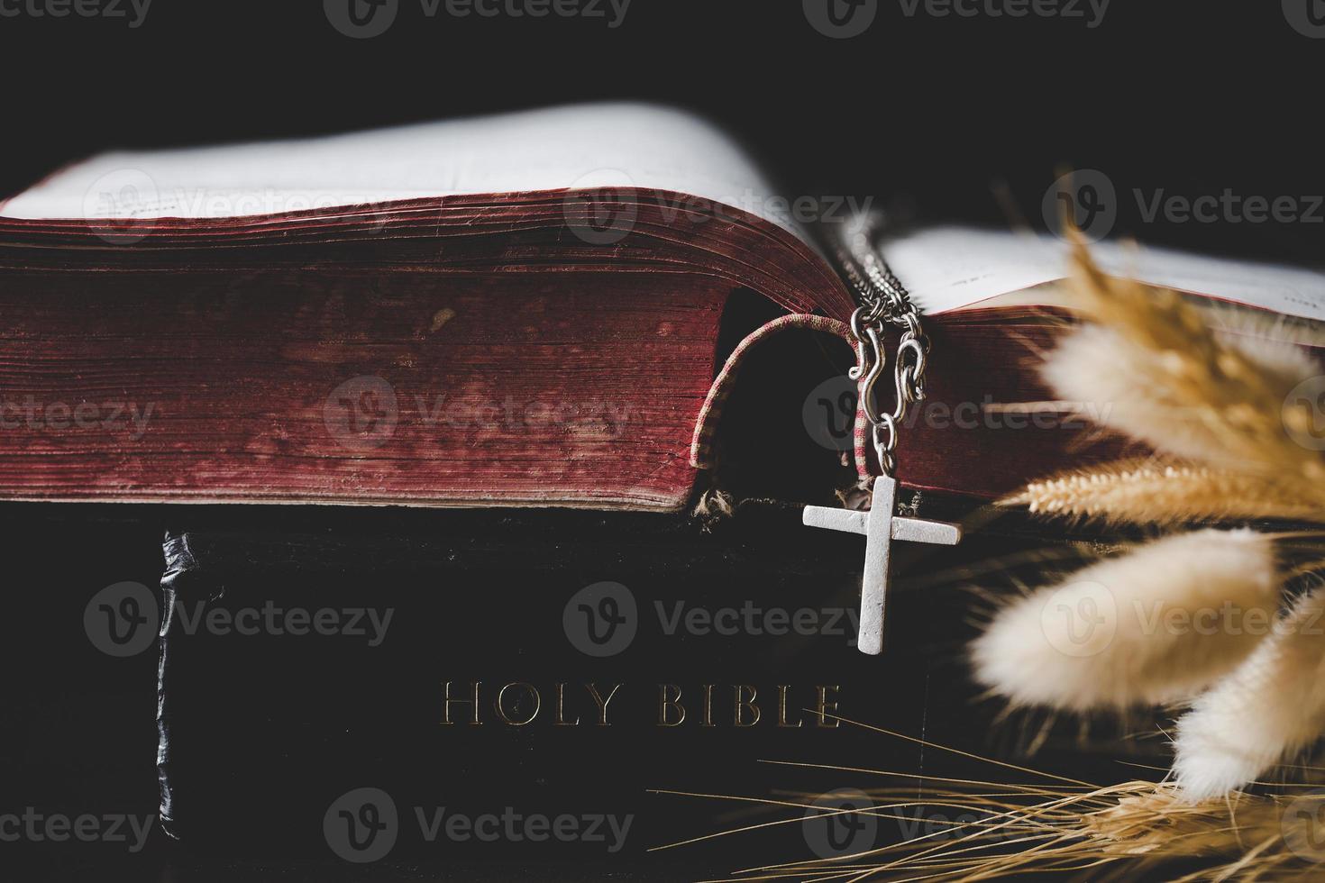 Holy bible book with cross or crucifix on old black wooden background. Christian catholic with protestant pray and study in church. Concept of cognition about faith god and religion, jesus spiritual. photo