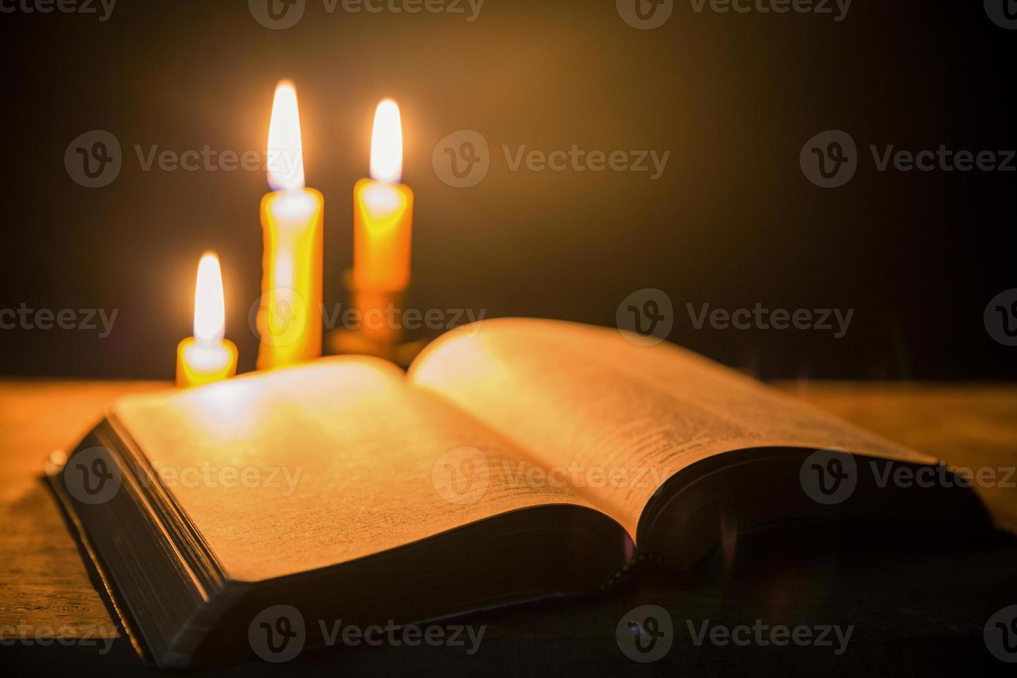 Light candle with holy bible and cross or crucifix on old wooden background in church.Candlelight and open book on vintage wood table christianity study and reading in home.Concept of christ religion photo