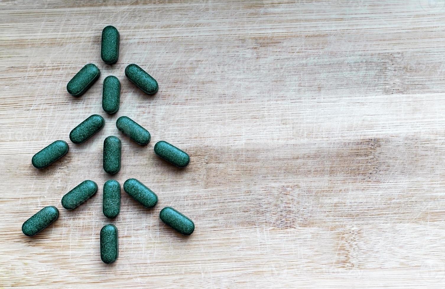 Pills of chlorella, spirulina or barley grass in the shape of a herringbone or christmas tree on a light wooden background with a copy space photo