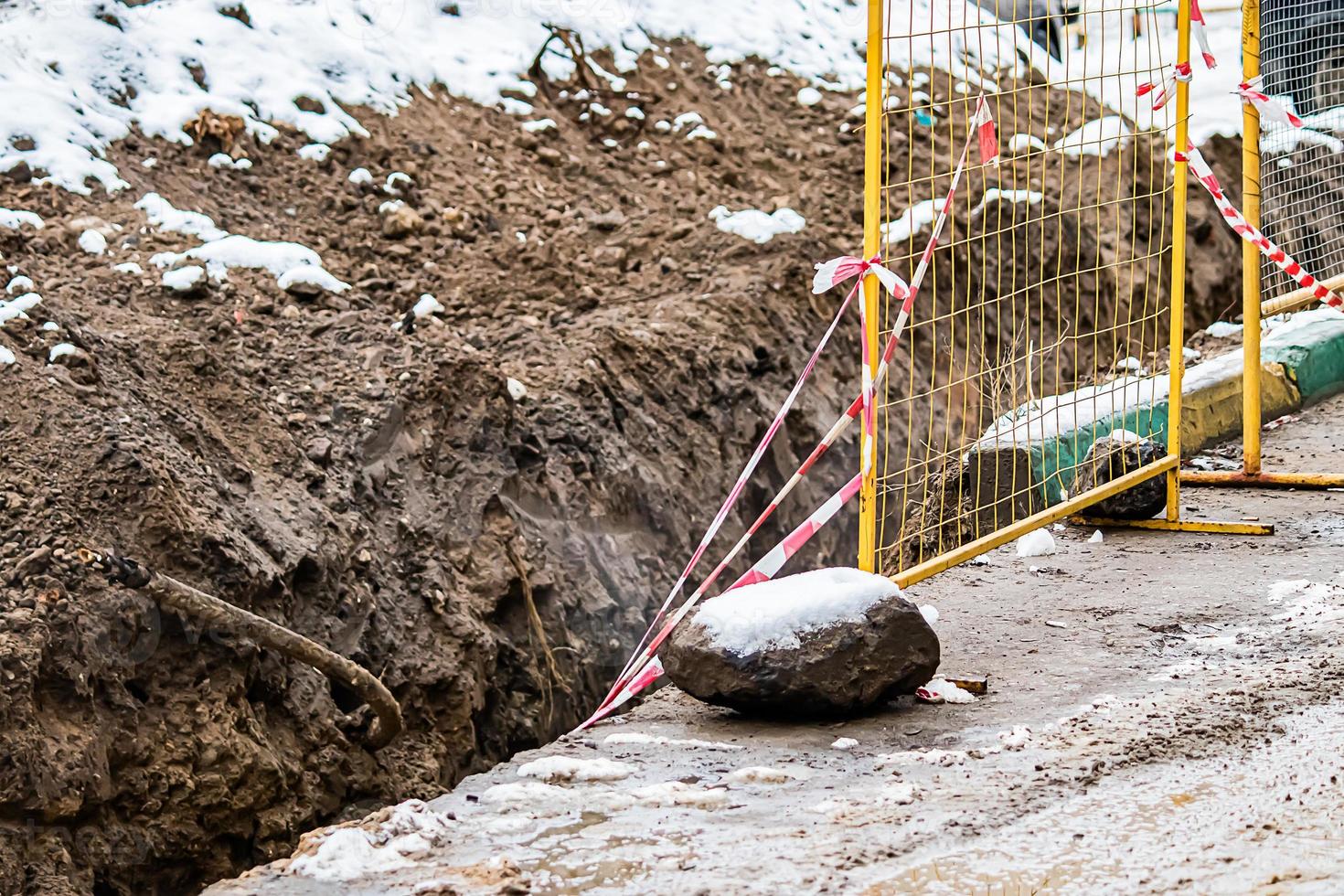 Repair of underground utilities in winter. Ditch in  ground, fenced off with grate. Abandoned construction site. photo