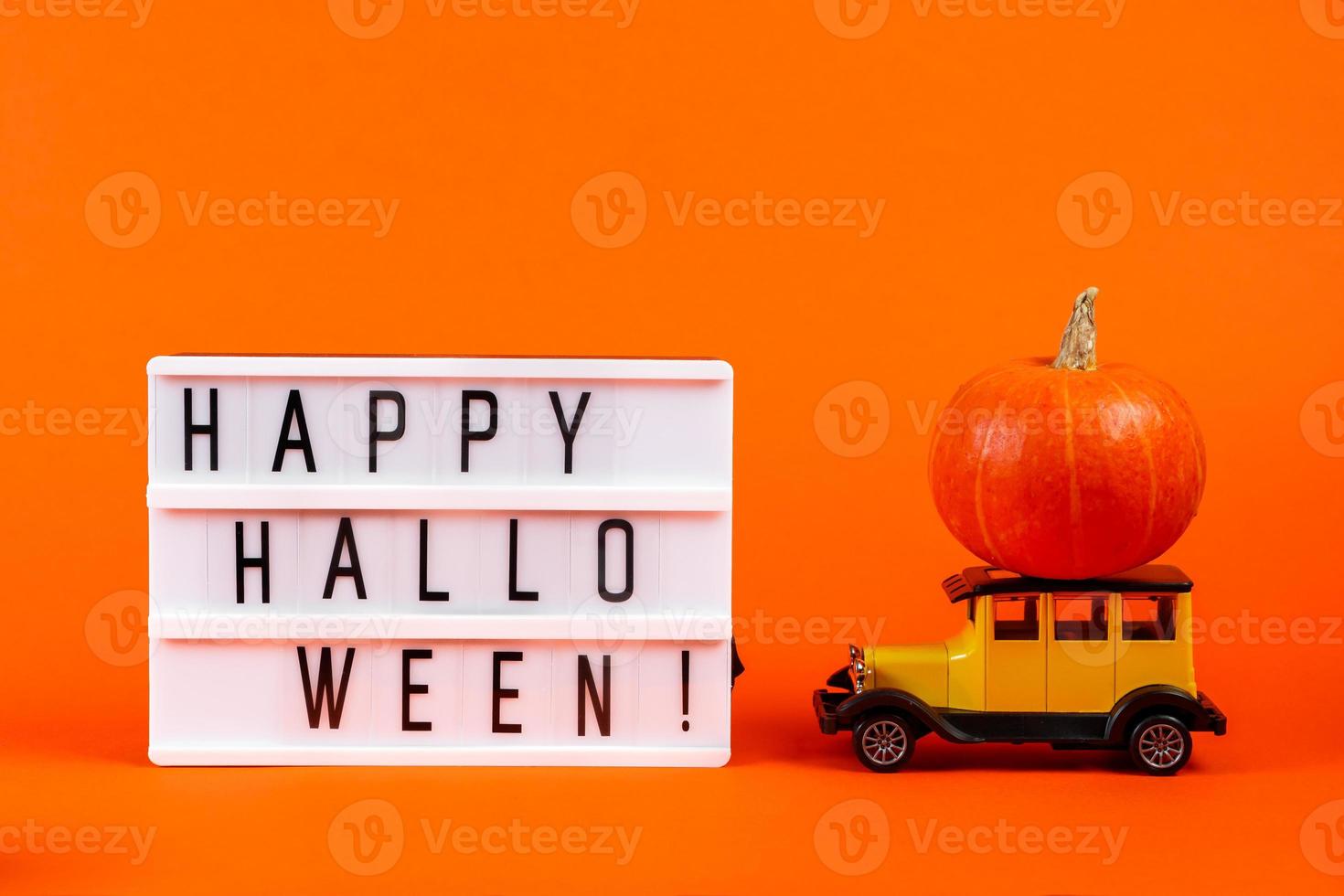 Retro toy car with a pumpkin on an orange background. Halloween and autumn harvest concept. photo