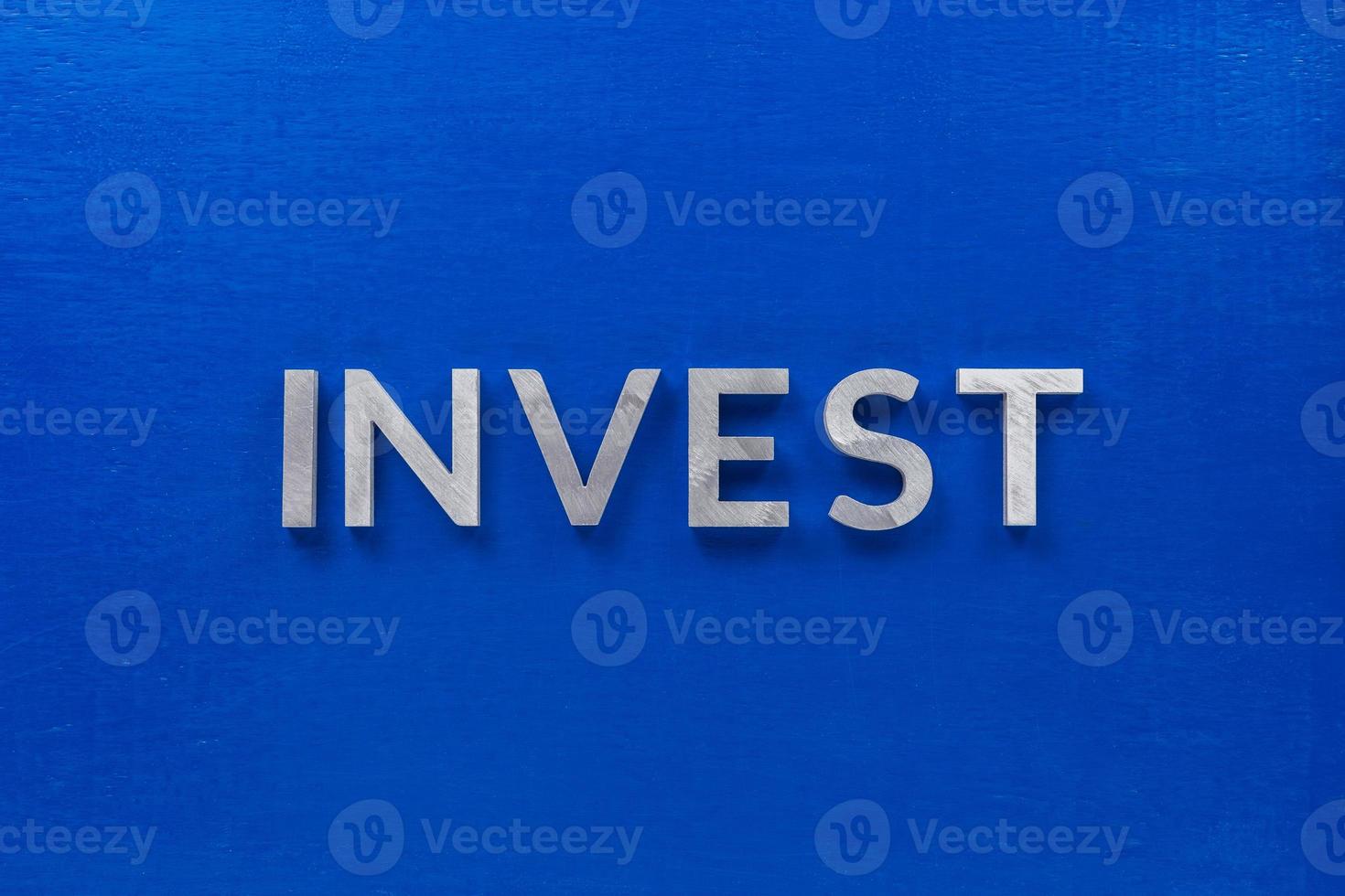 the word invest laid with silver metal characters on blue painted wooden board in central flat lay composition photo