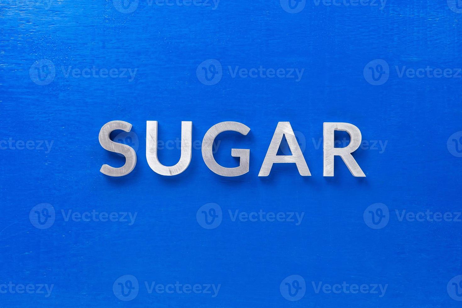 the word sugar laid with silver metal characters on blue board in flat lay centered composition photo
