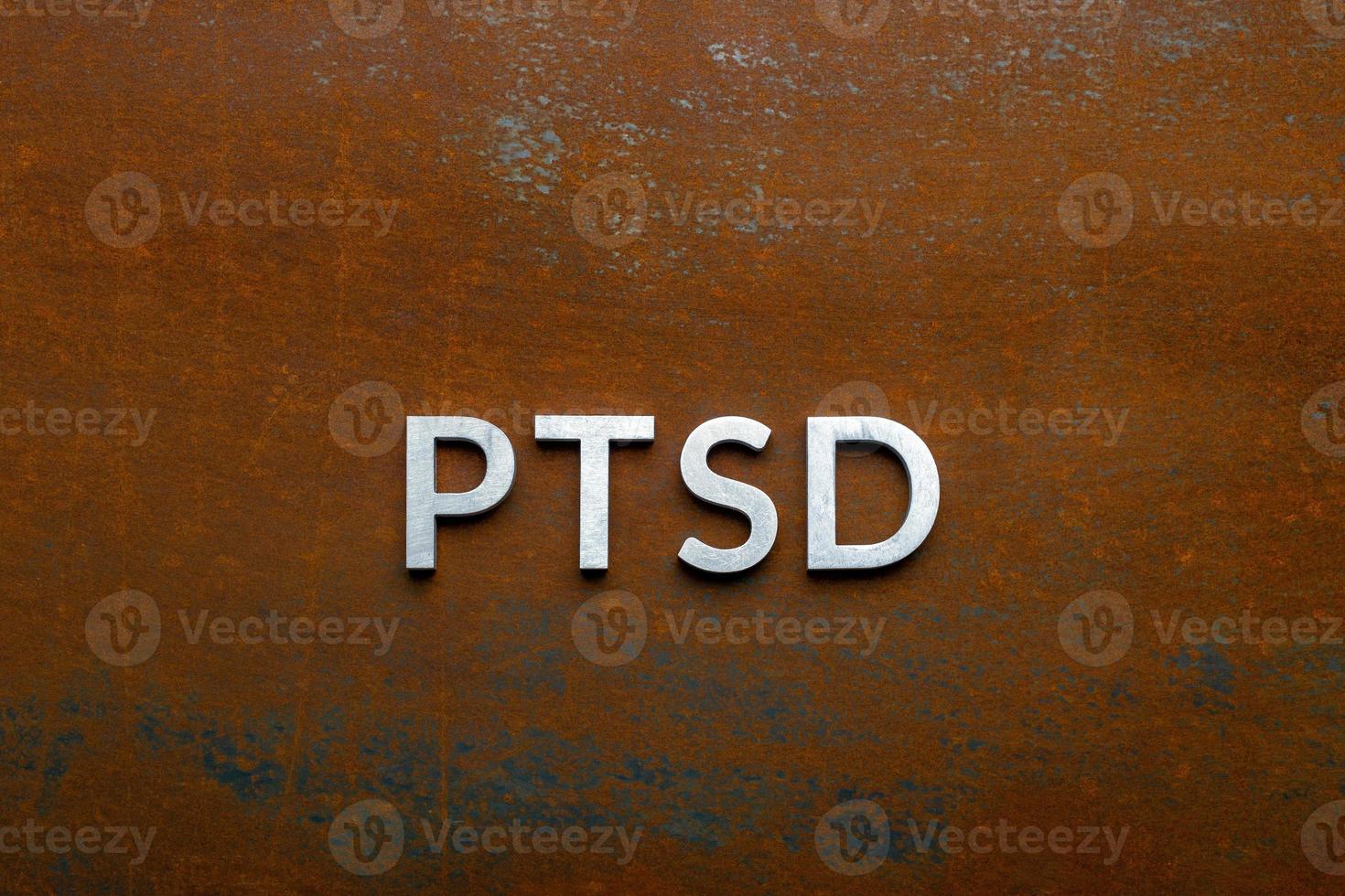 the word PTSD laid with silver metal letters on flat rusted steel sheet background in directly above perspective photo