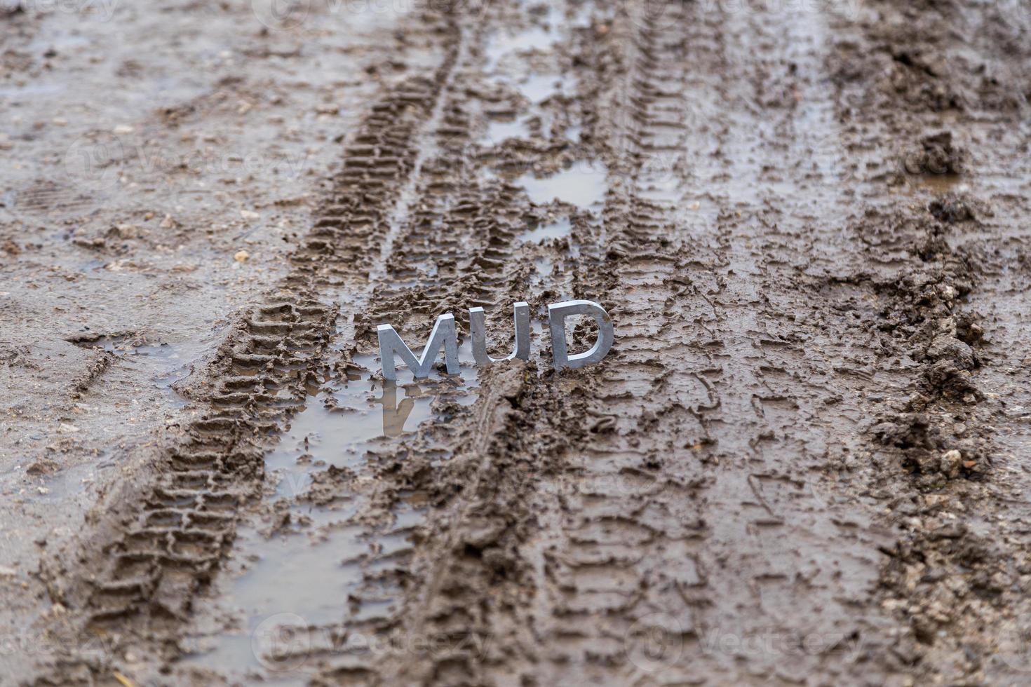 the word mud composed of silver metal letters on wet dirt surface photo