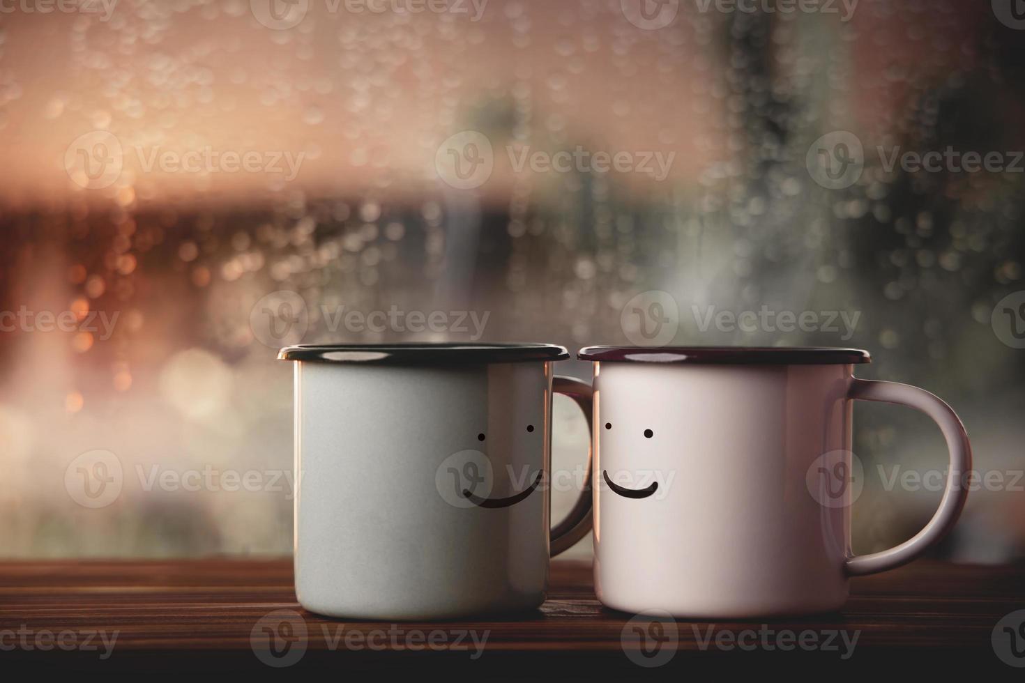 Love and Valentines Day Concept. Couple of Coffee Cup with Smiling face by Glass Window in House. Happiness, Romantic or Positive Mind on Rainy Day photo