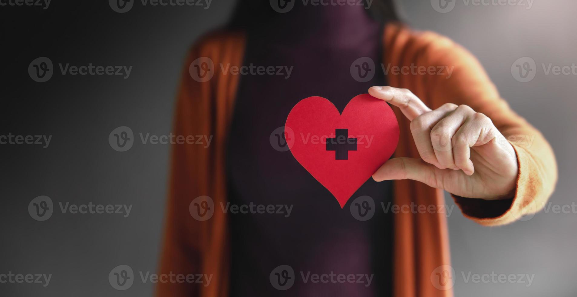 Love, Health Care, Donation and Charity Concept. Close up of Volunteer Woman Holding a Heart Shape with Cross Sign Paper. presenting to Camera photo