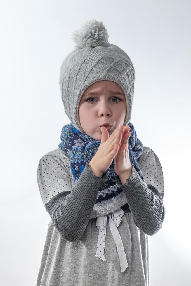 niña molesta con un sombrero gris envuelto en una bufanda sobre un fondo blanco, esperando el frío invierno. foto