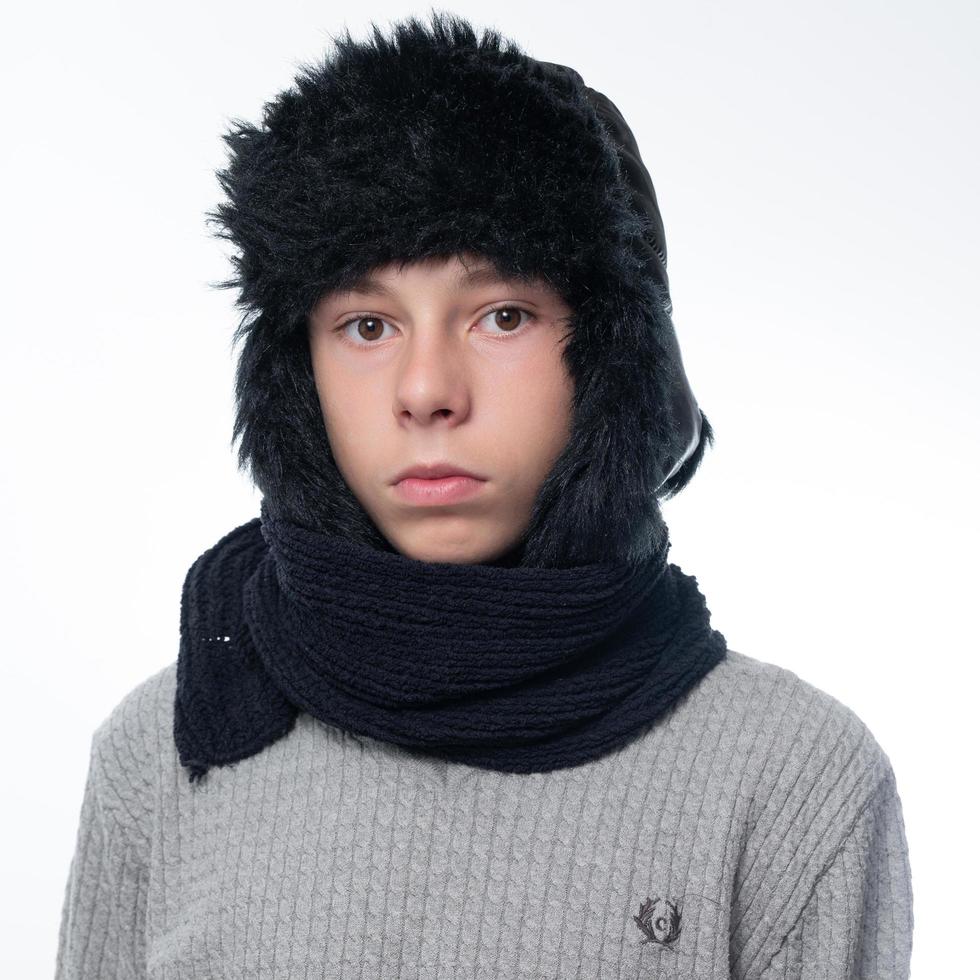 Portrait of a child in a winter hat with earflaps and a knitted scarf on a white background. photo