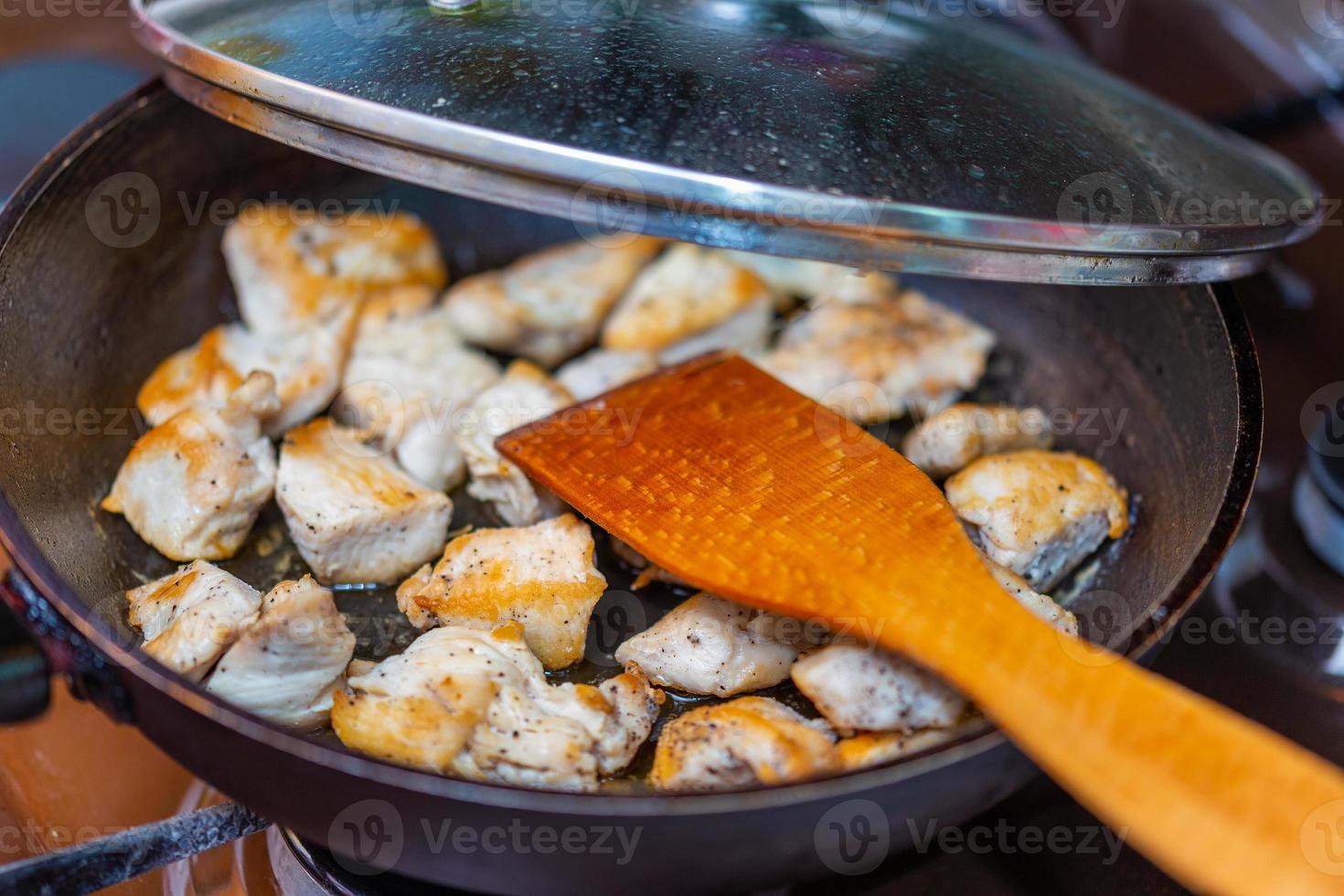 fried chicken in a open pan with ground black pepper and wooden kitchen spatula photo